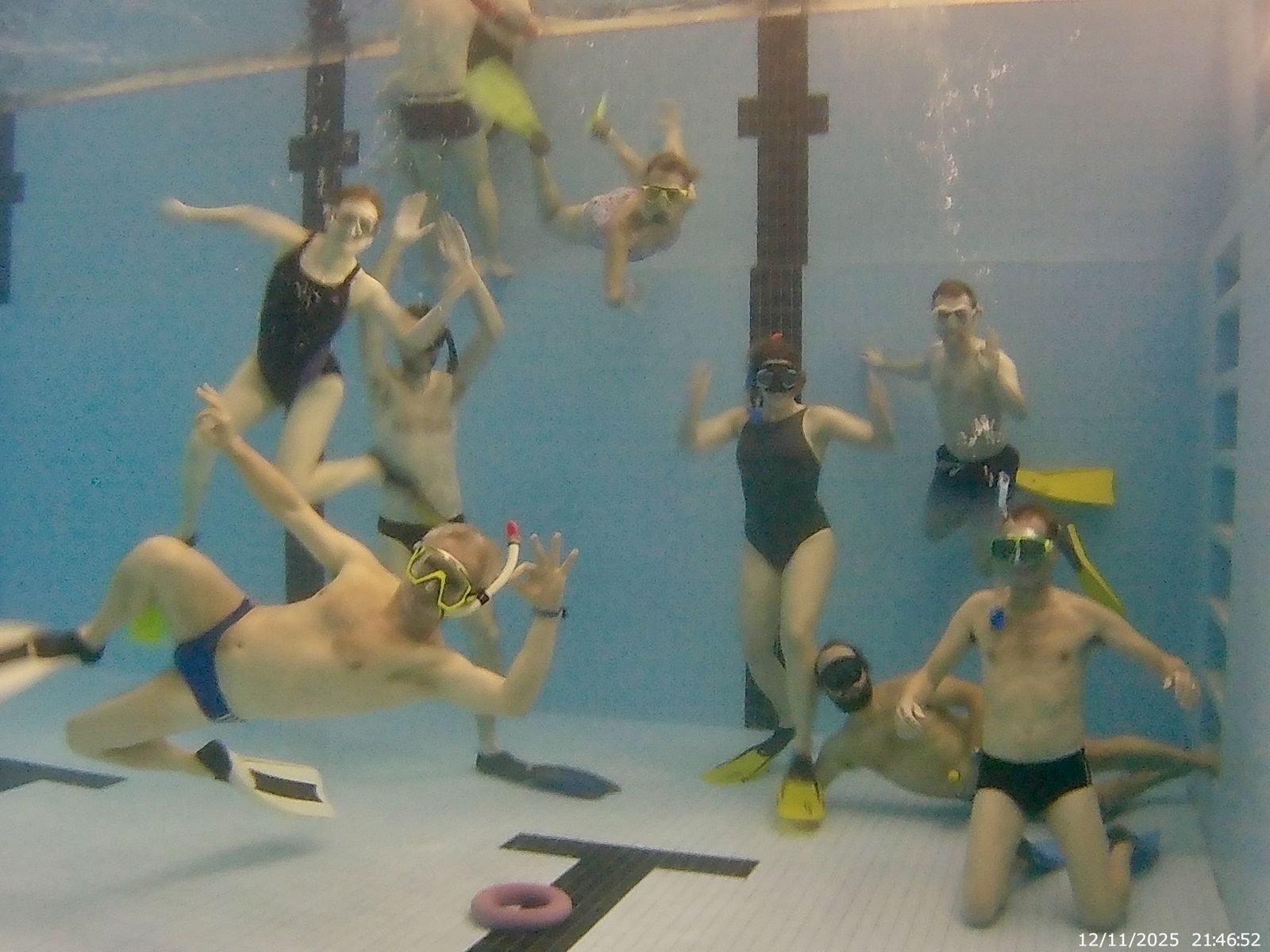Gruppenfoto unter Wasser im Hallenbad: Vereinsmitglieder mit Masken, Schnorcheln und Flossen winken in die Kamera.