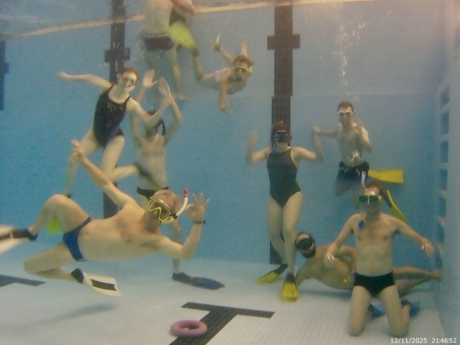Gruppenfoto unter Wasser im Hallenbad: Vereinsmitglieder mit Masken, Schnorcheln und Flossen winken in die Kamera.